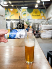 Person pouring beer from a can into a glass at a bar with a blurred background