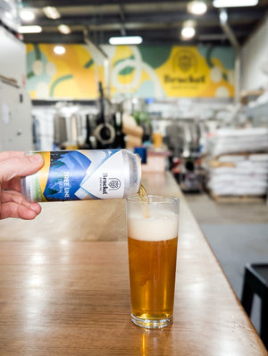 Person pouring beer from a can into a glass at a bar with a blurred background